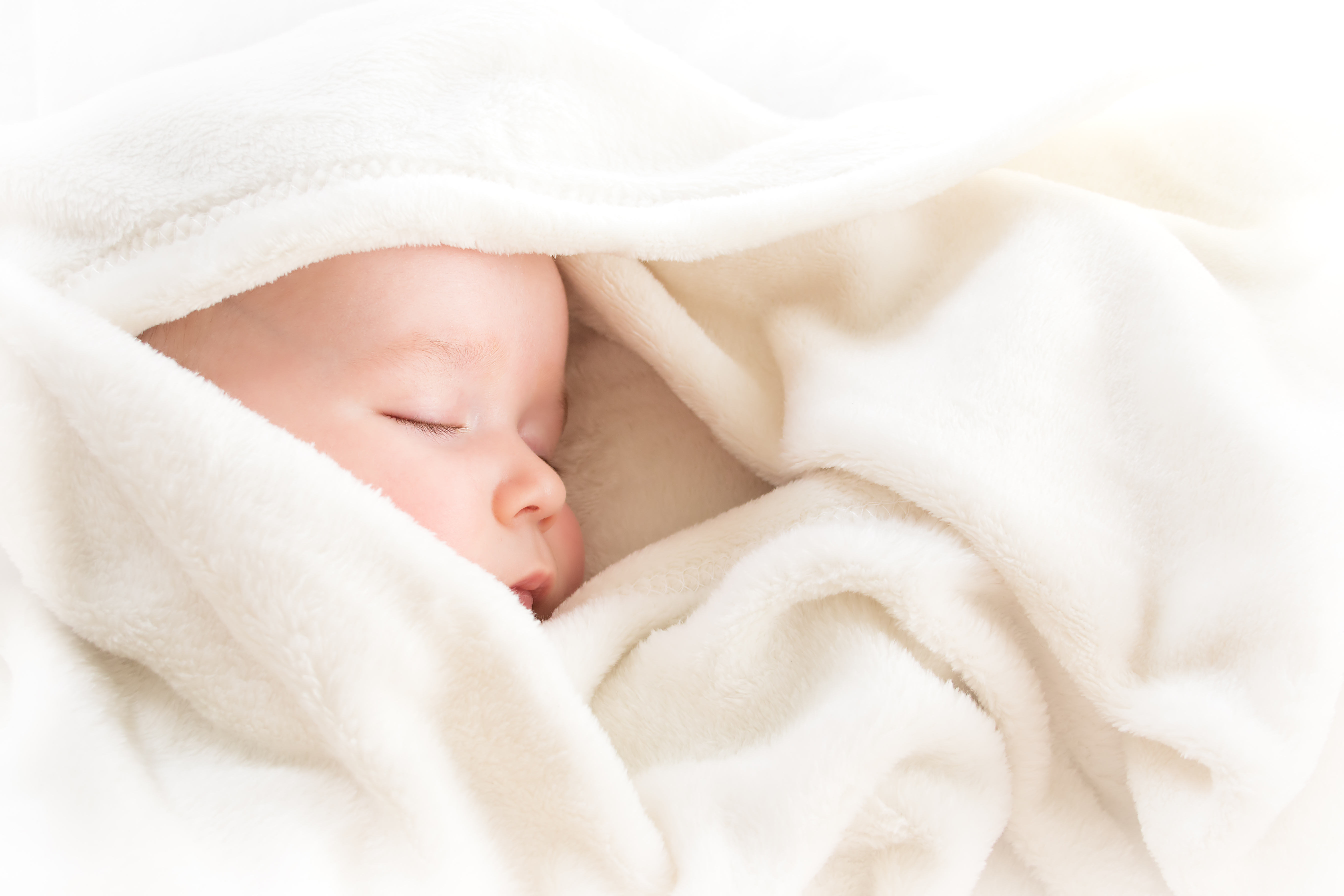 A baby asleep on their side wrapped in a blanket that is covering the baby's head and part of their face.