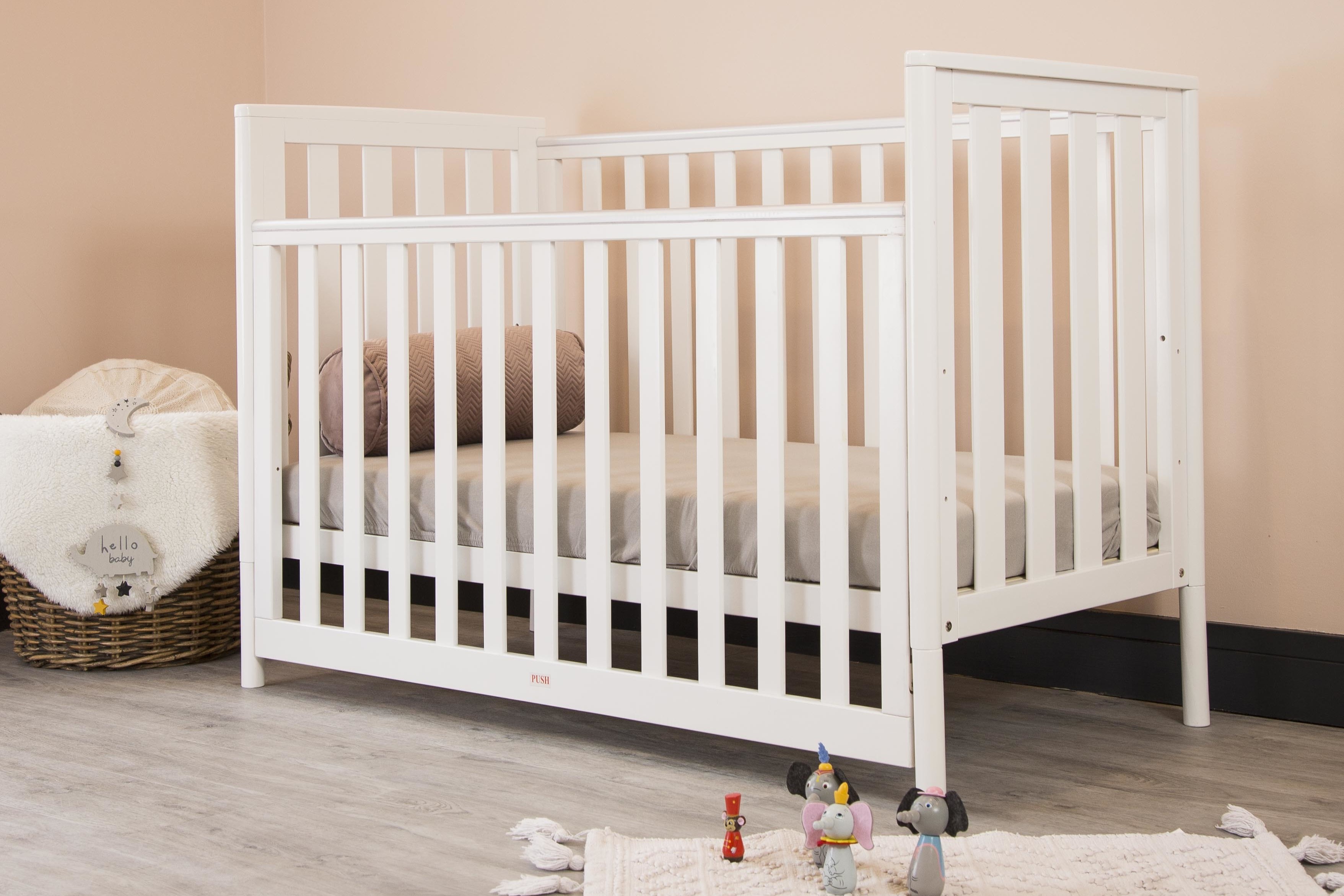 A drop-sided crib with a firm, snug-fitting mattress and a pillow.