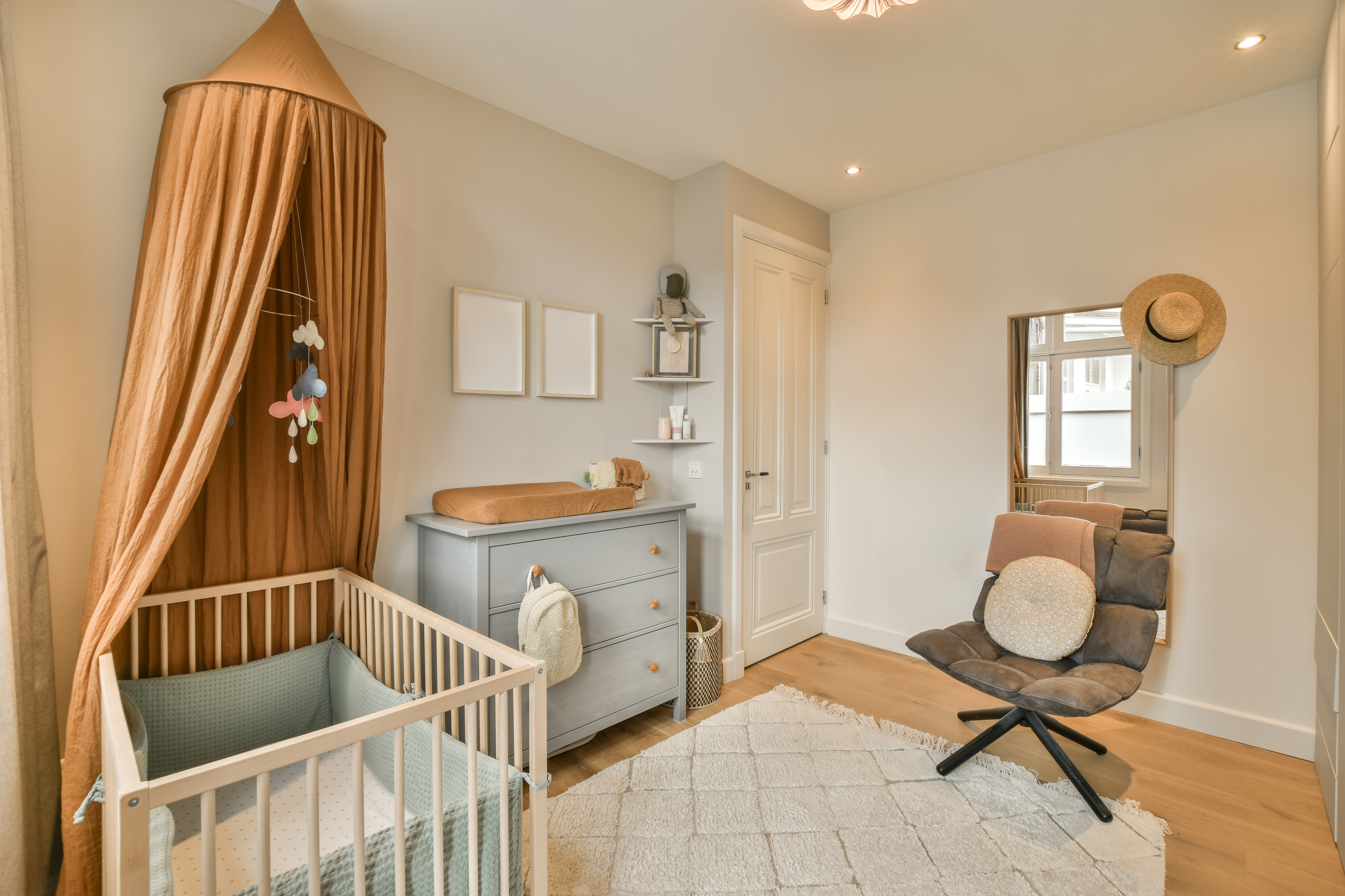 A nursery with a crib with bumper pads and a canopy hanging over the crib.