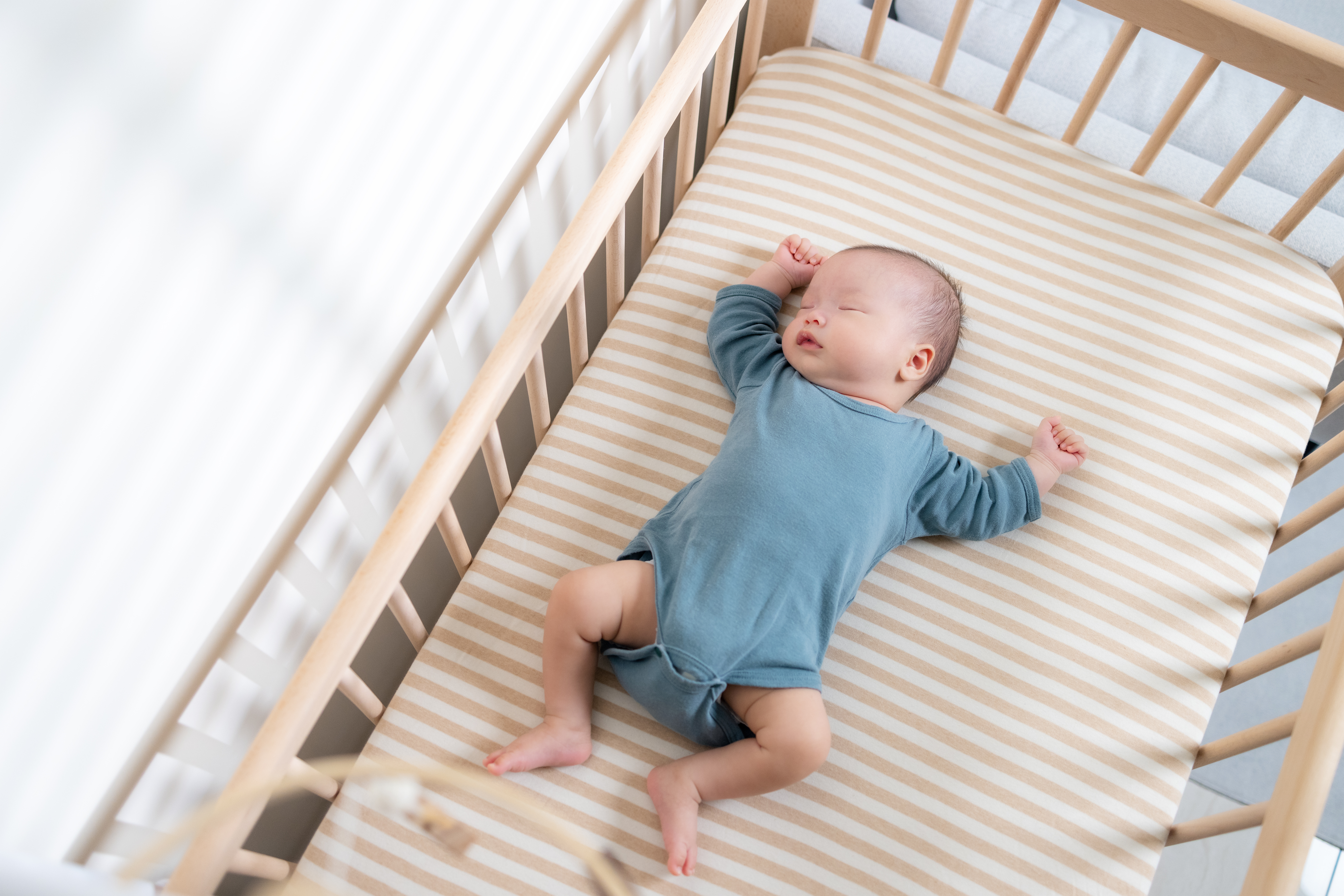 A baby asleep on their back in an empty crib.