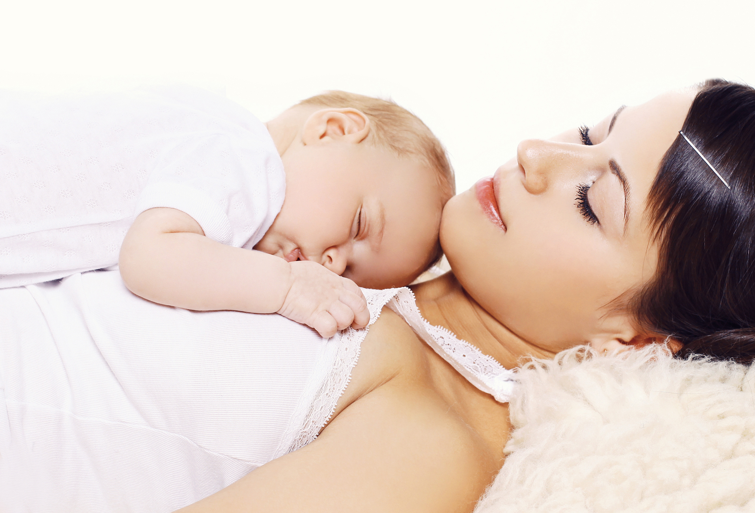 A baby asleep on their stomach on top of their sleeping caregiver.