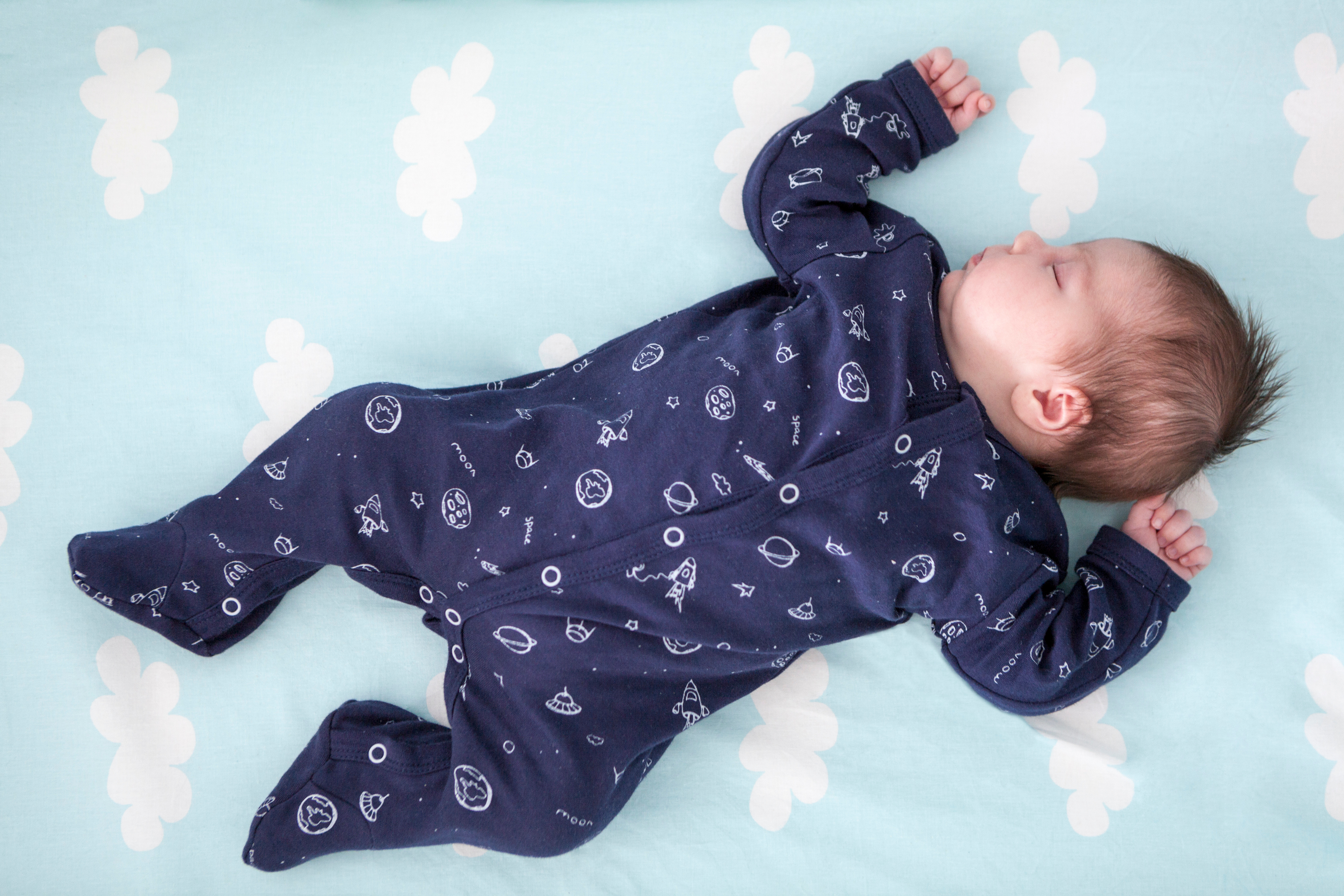 A baby asleep on their back wearing a sleeper.